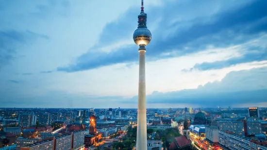 Berlin television tower at dusk, surrounded by the skyline and illuminated buildings.
